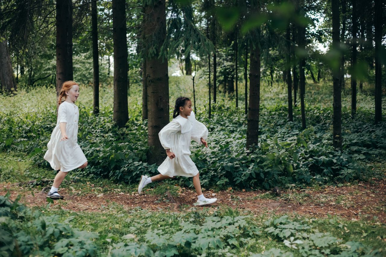 Mastering the First Impression: Your intriguing post title goes here Young girls in white dresses joyfully running through a lush green forest path.